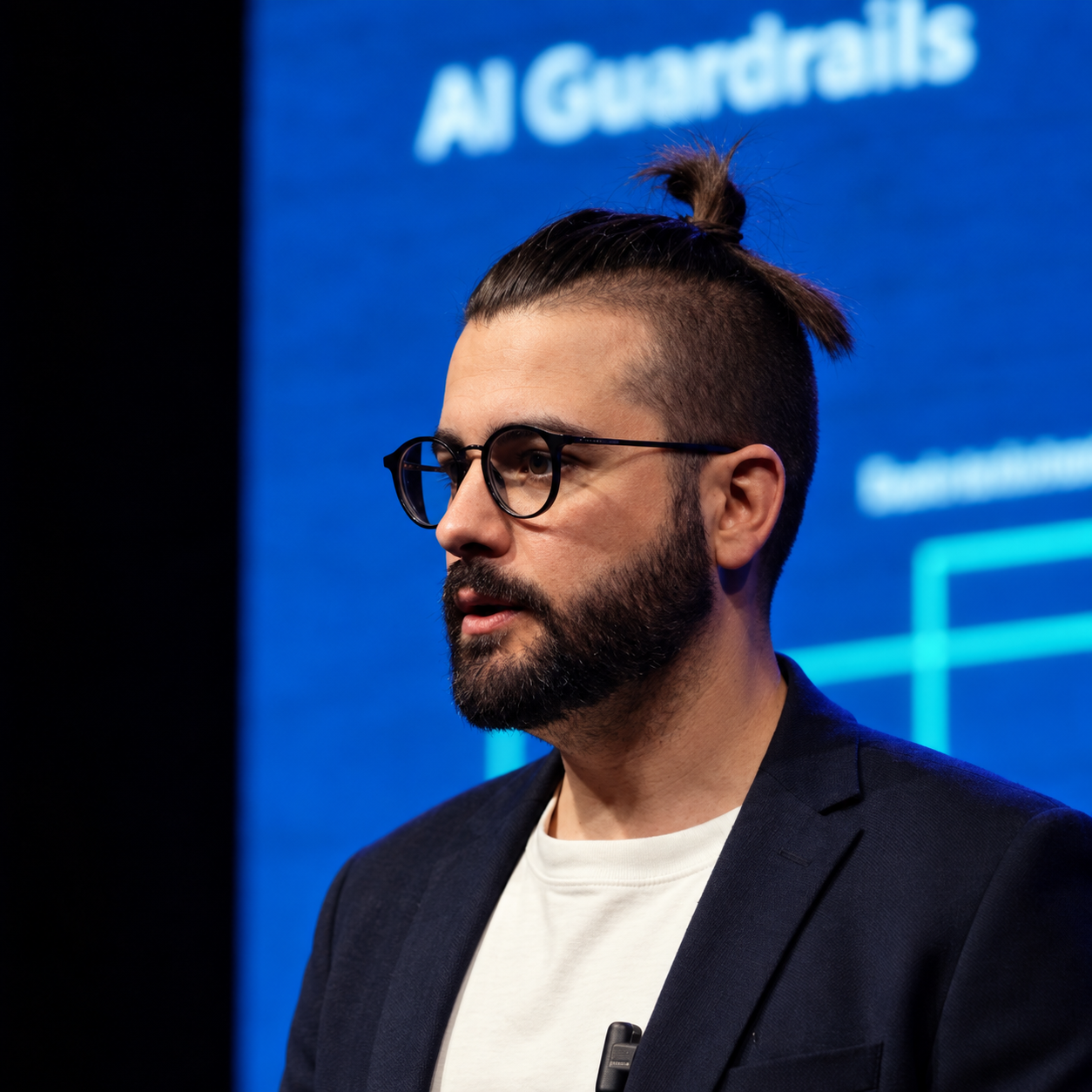 Portrait of Marcos Rezende wearing glasses and a dark blazer against a blue AI Grenadines event backdrop.