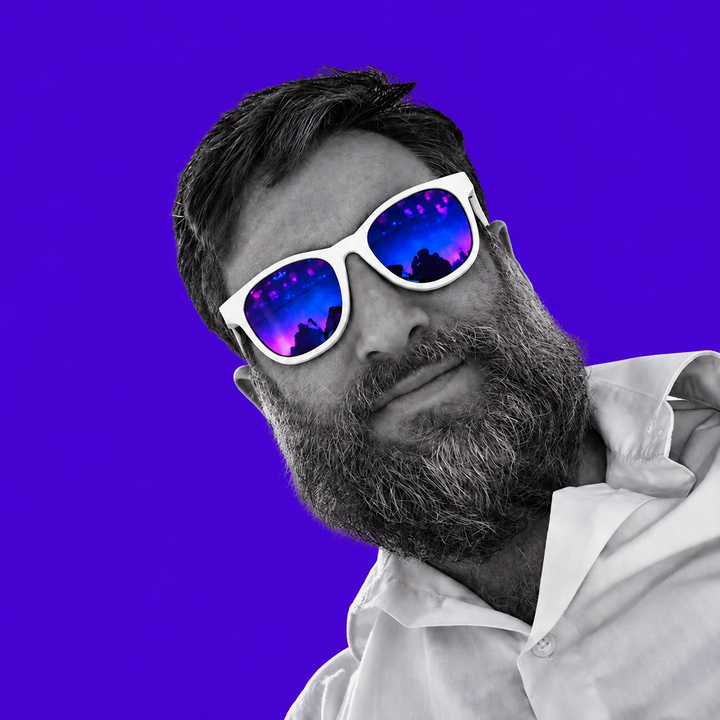 Portrait of Paul Stefaan Mooij wearing white-framed smart glasses, with stage lights reflected in the lenses, against a violet background.