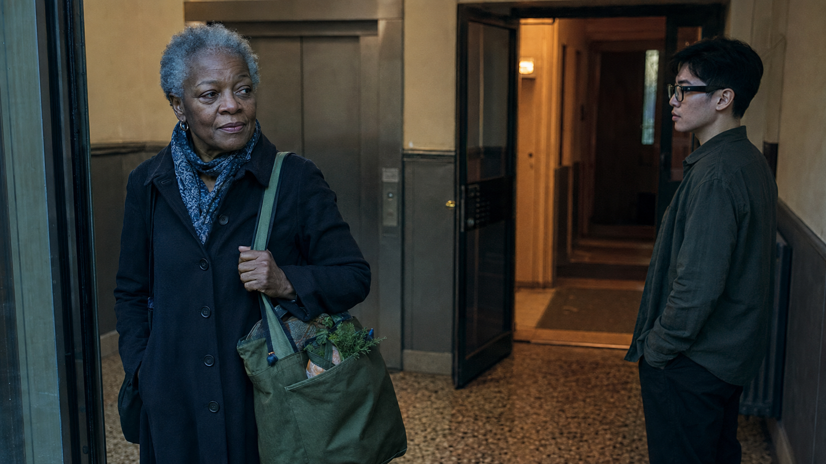 Two people standing near an apartment entrance, one carrying a green bag and the other wearing glasses, illustrating everyday privacy boundaries.